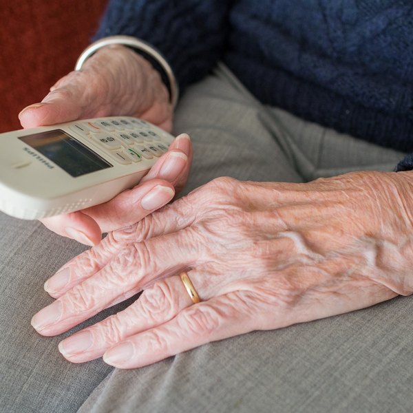 Hände einer alten Frau halten ein Telefon