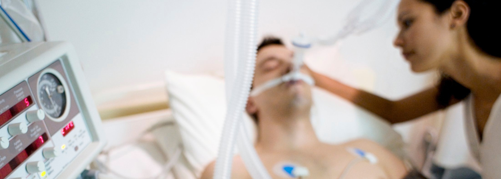 Eine intensivbed&uuml;rftige Person liegt in einem Bett, an der rechten Seite steht eine Angeh&ouml;rige