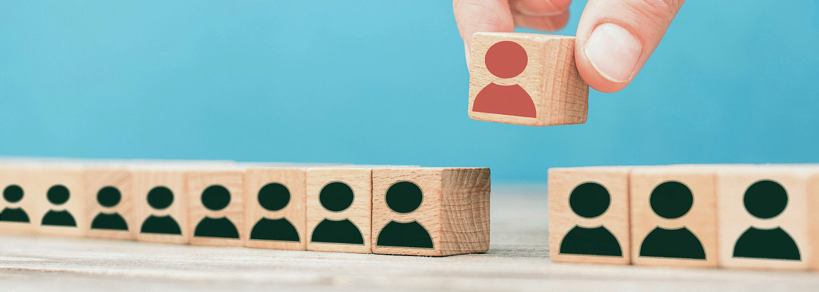 Symbolische Darstellung des Personalmanagements: Eine Hand wählt gezielt einen Holzbaustein mit einer roten Person aus einer Reihe neutraler Figuren aus. Ggf. Bildunterschrift: Personalmanagement: Die richtige Person an der richtigen Stelle – strategische Entscheidungen für ein starkes Team.
