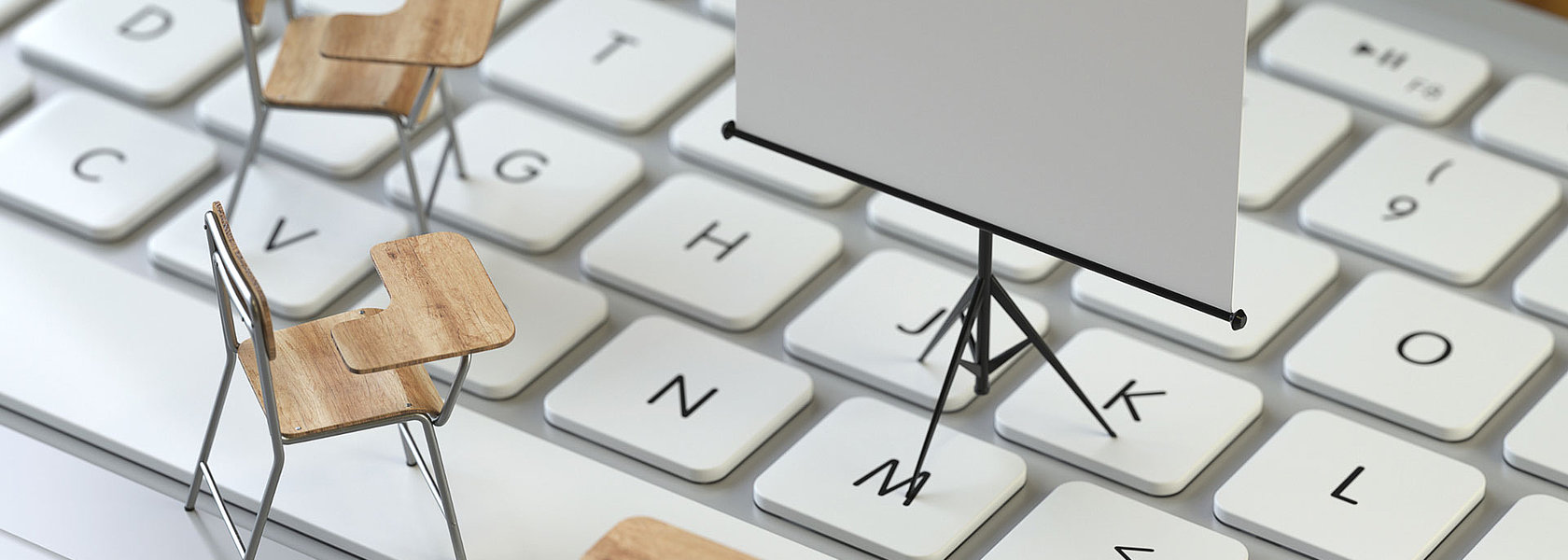 Miniatur-Schulstühle und eine Leinwand auf einer Computertastatur, die Fortbildungen im digitalen und persönlichen Dialog repräsentieren.