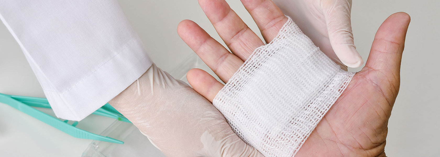 Eine medizinische Fachkraft mit Handschuhen versorgt eine Handwunde mit einem sterilen Verband.